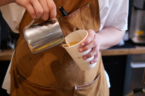 The coffee machine is frothing milk. Barista's hands hold a jug of milk