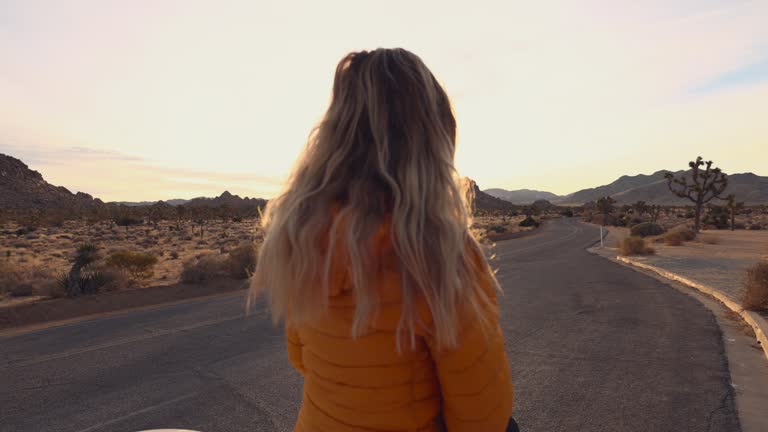 Female traveller sitting on top of car hood enjoys sunrise on the side of the road