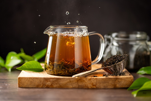 Cup of green tea and dry loose leaves, dark moody background