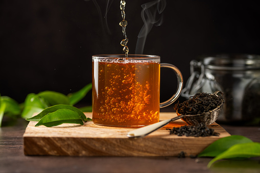 Cup of green tea and dry loose leaves, dark moody background