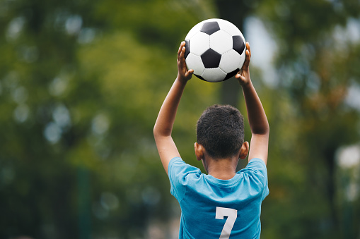 Soccer Throw In During Children Sports Game. Little Boy Holding Soccer Ball in Hands. Kids Playing in Football League. Boy in Soccer Blue Jersey With Number Seven