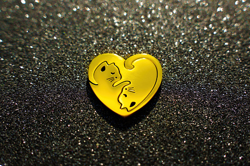 Heart-shaped union of two golden halves, forming an embracing pair of kitties, placed on a sparkling black backdrop.