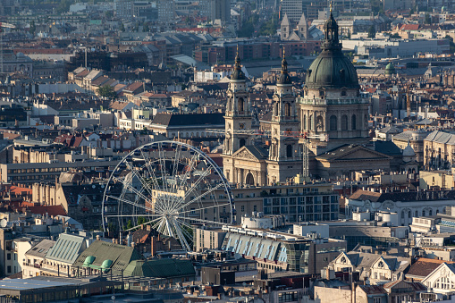 A birds eye view of the St Stephen Basilica with its twin towers and large dome and the Ferris Wheel.\nBudapest, Hungary