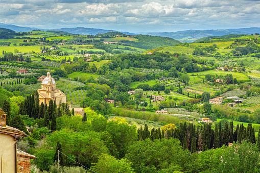 In the serene Italian countryside, cultivated land stretches across rolling hills, adorned with olive tree plantations and elegant cypress trees. Charming farms dot the landscape, contributing to the agricultural richness of the region. Amidst this idyllic scene, the Church of San Biagio stands proudly, adding a touch of historical and spiritual significance to the picturesque setting.