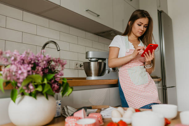 istock Young Woman With Vegetables Smiling While Using Mobile Phone In Kitchen 1939652267