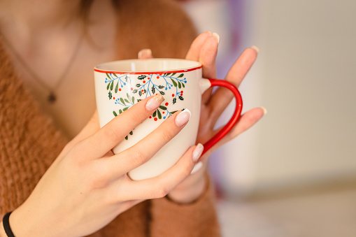 Warm and delightful scene of a lady enjoying a cup of coffee in close-up, featuring a festive mug with Christmas colors.