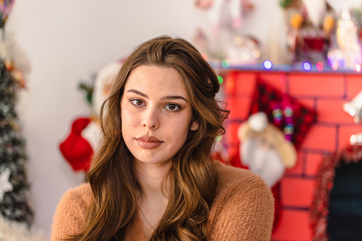 Close-up of a lovely young woman in a cozy brown sweater, surrounded by festive Christmas decorations.