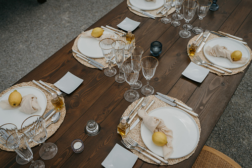 Place setting, plates and glasses set up on wooden table for outdoors party.