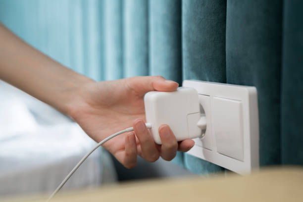 istock A persons hand is captured in the moment of inserting a two-pronged white electrical plug into a standard wall-mounted power socket, suggesting an indoor domestic or office setting. 1939687490