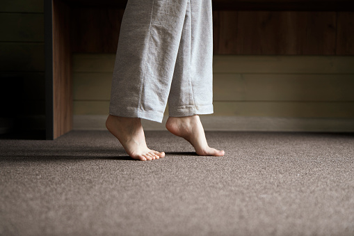 A close-up view shows bare feet standing on a carpeted floor, likely indicating the warmth from a heating system in a residential setting.