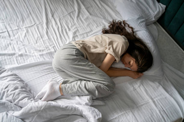 istock A woman is captured taking a nap, curled up in a bad wrong on a white-sheeted bed, suggesting a midday or early morning rest. 1939688595
