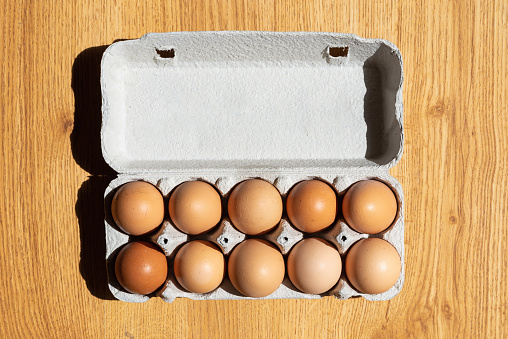 Fresh chicken eggs background. Brown eggs in craft carton pack on hay at rustic wood table.Top view. Natural healthy organic food.Chicken eggs in carton box on wooden table.