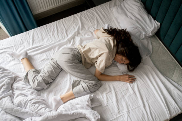 istock A woman is captured taking a nap, curled up in a bad wrong on a white-sheeted bed, suggesting a midday or early morning rest. 1939688605