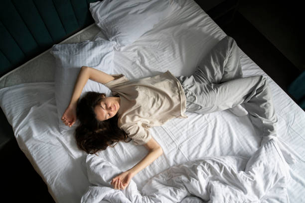 istock A woman is captured taking a nap, curled up in a bad wrong on a white-sheeted bed, suggesting a midday or early morning rest. 1939688606