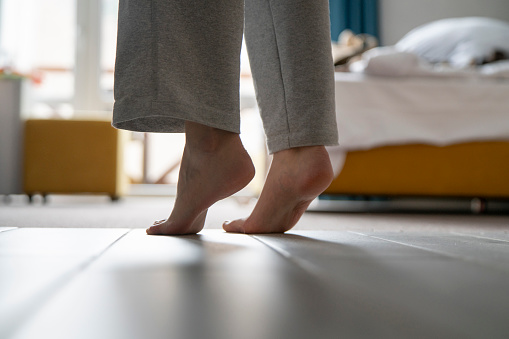 A close-up view shows bare feet standing on a carpeted floor, likely indicating the warmth from a heating system in a residential setting.