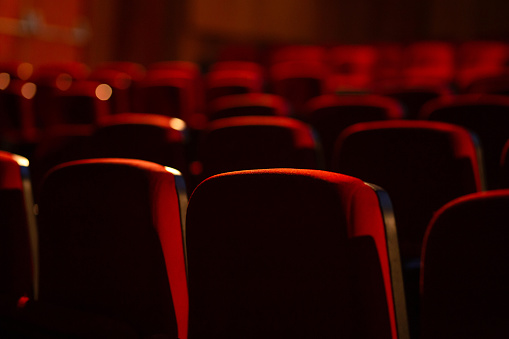 Detail of an empty theater. Several rows of red armchairs photographed from behind. Photography with narrow focus.