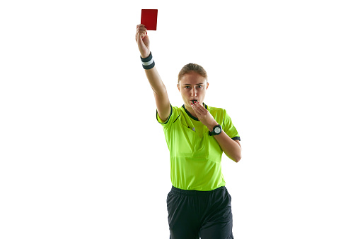 A Referee, wearing a whistle, a  black and white striped shirt, squeezinging a deflated football and holding a penalty flag in the other hand, against a white background