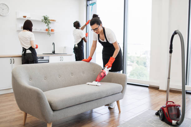 istock Full length of multiethnic young cleaner vacuuming sofa. 1939714914