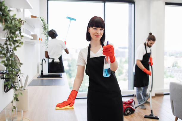 istock Caucasian janitor in apron and gloves having fun, sprays detergent into camera 1939716597