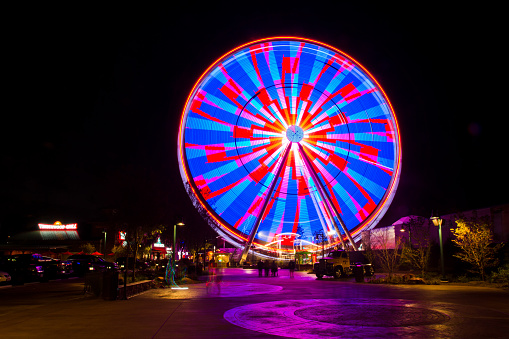 Vibrant ferris wheel illuminates the night sky in Gatlinburg, Tennessee, creating a mesmerizing display of colorful streaks. Experience the excitement of this lively entertainment district.