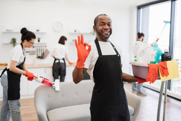 African man professional cleaning worker pointing on bucket with detergents.