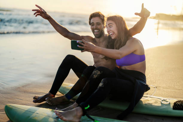 A silly couple on surfboards taking selfies on a shore.