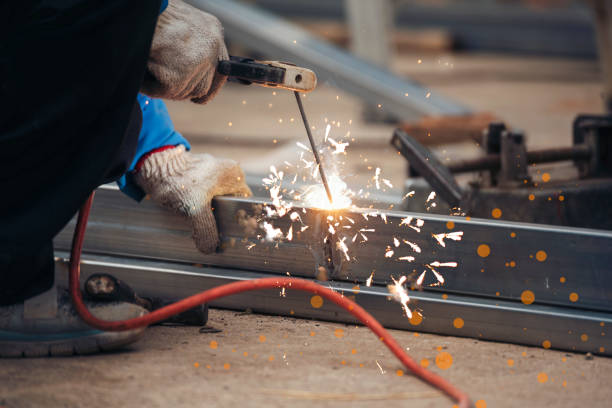 Construction Worker hands using Welding machinery iron metal sparking. Men hands wear protective glove Hot flame metal work cutting fire iron workshop. Locksmith use Welding machine cut metal process