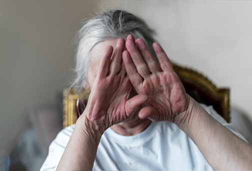 portrait of an elderly woman who covered her face with her hands, she is stressed or sad