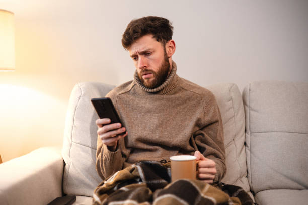 istock The man is sick with a cold at home on the sofa, uses a smartphone 1939753028