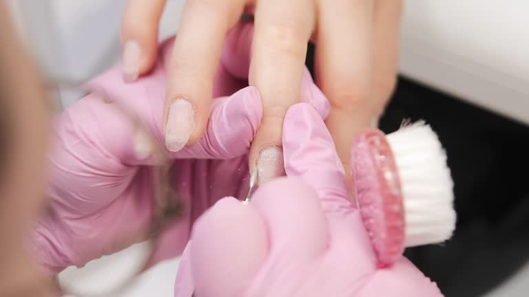 A manicurist prepares nails for a manicure in a salon, working on the cuticle. Handheld shot, close up.