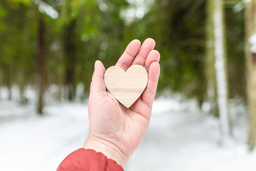 Man palm holding heart on blurred winter forest trees.Valentine's day concept
