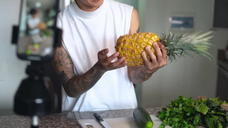 Happy young man recording a video vlogging about vegetable juice in the kitchen at home.