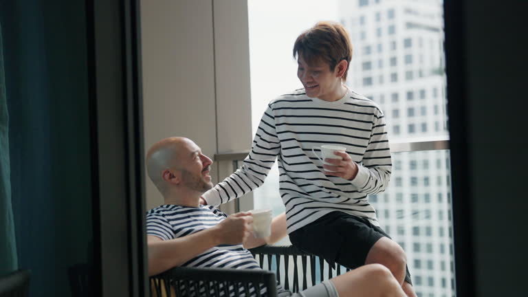 A LGBT male couple happily drinks coffee in the morning on the balcony.