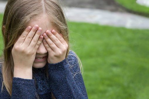 Sad little girl covering her eyes with her hands. Shallow depth of field.