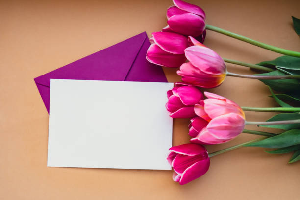 istock Empty white envelope copy space for your text or design with beautiful pink tulip bouquet on beige background. Template mock up for holiday spring greeting card. Top view Flat lay blank paper Feminine concept postcard 1939828174