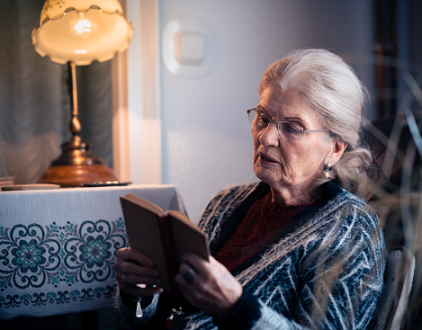Old woman sitting at home and reading a book