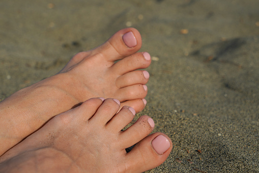 Close-up - female feet on the background of sand on the beach. Woman feet close-up relaxing on beach, enjoying sun