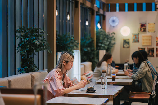 Asian Chinese young woman reading phone text messaging in restaurant