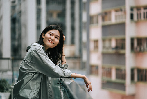 Asian Chinese young woman leaning on balcony looking at camera smiling