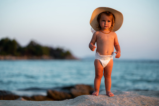 Full length of a little girl with a sun hat is standing on the beach