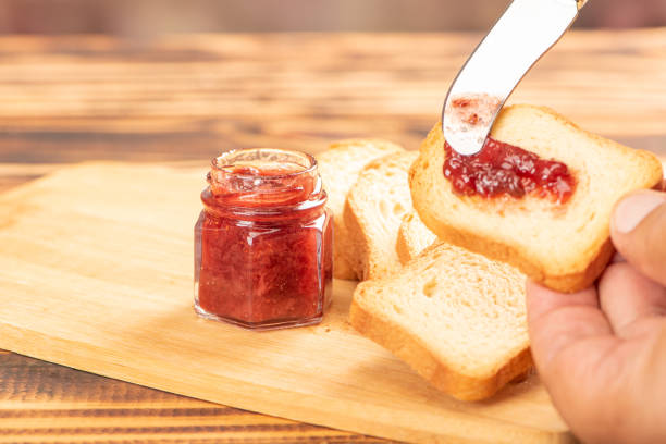 istock Jam and toast, hand spreading jam on toast with knife on rustic wood. Selective focus. 1939874498