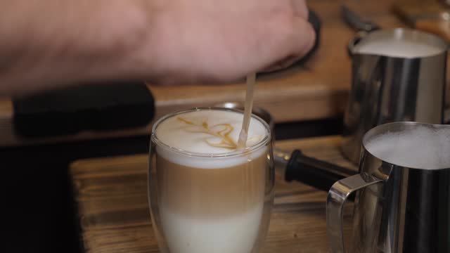 A barista pours milk into a cup and creates cappuccino art in a coffee shop.