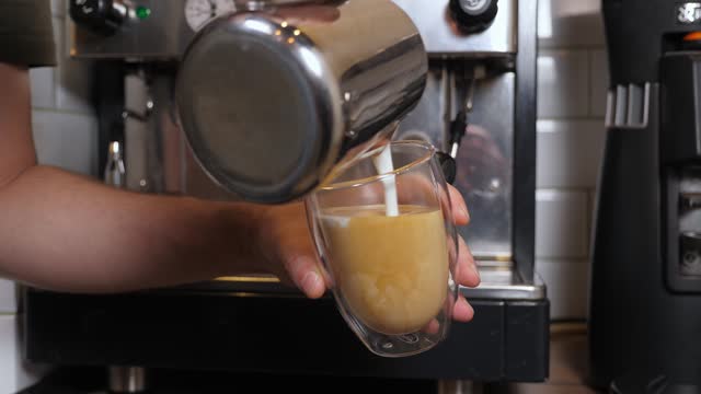 A barista pouring whipped milk into a cup of coffee creating a milk pattern.