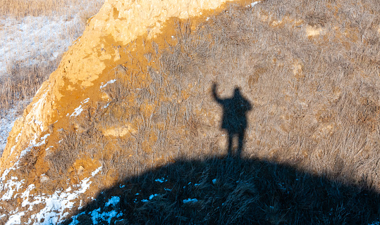 Black shadow, silhouette of a man with a raised hand on the shore of the estuary in winter
