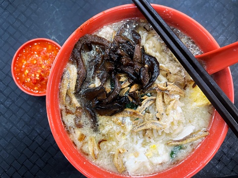 Overhead view of a bowl of cooked Chinese noodle with dried anchovies and mushrooms toppings and accompanied ground chilli sauce