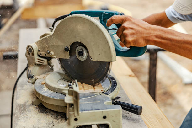 istock Close up of worker's hands manipulating cutting machine and cutting wooden board on site. 1939901451