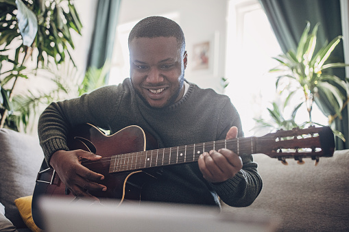 A joyful adult engages in music, playing the guitar and laughing in a cozy home atmosphere.