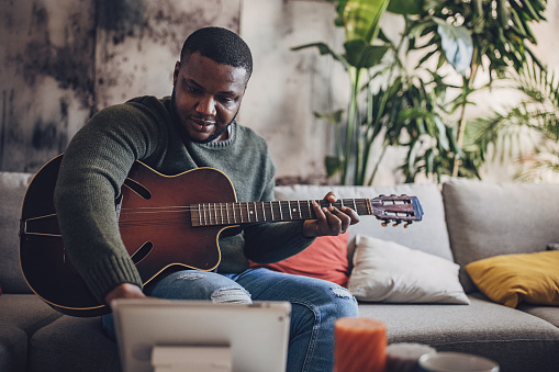 A joyful adult engages in music, playing the guitar and laughing in a cozy home atmosphere.