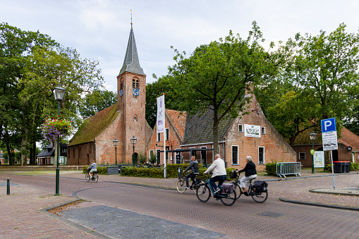 Roden, The Netherlands - August 29, 2023: Tourist passing picturesque church of Roden surrounded by oak trees, municipality Noordenveld in Drenthe The Netherlands