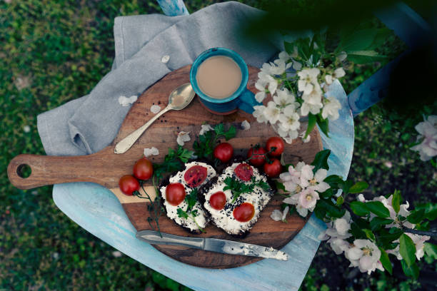 野菜、コーヒーカップ、花が咲いたボードの上で朝食に健康的な食事。庭での食べ物や飲み物。ランチタイムの田園風景。テーブルトップビュー。